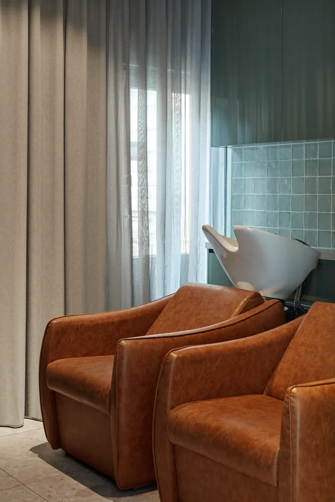 Teal-tiled wash area with sheer curtain and tan armchairs at Frankie Salon South Yarra