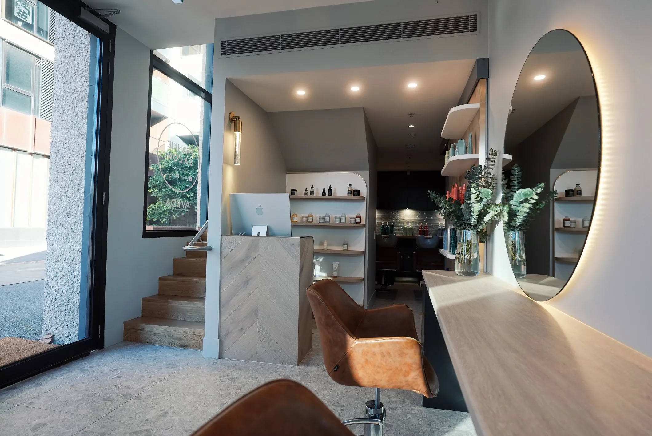 Richmond salon — long wood counter, round mirror, tan chair, marble detailing